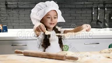 <strong>小美女</strong>戴着厨师帽玩面团的肖像，孩子在真正的厨房做饭。 4k